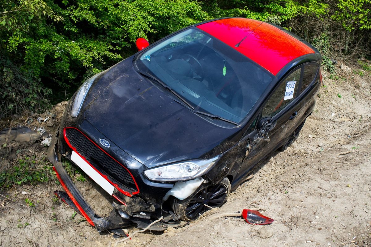 A damaged black and red car on a dirt road