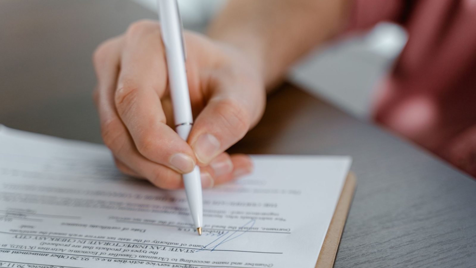 A hand writing a signature on a document with a ballpoint pen