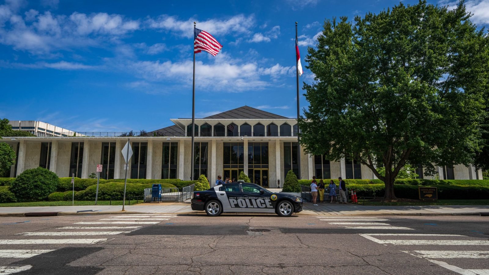 A government building facade with flags, with a police car in front on a sunny day