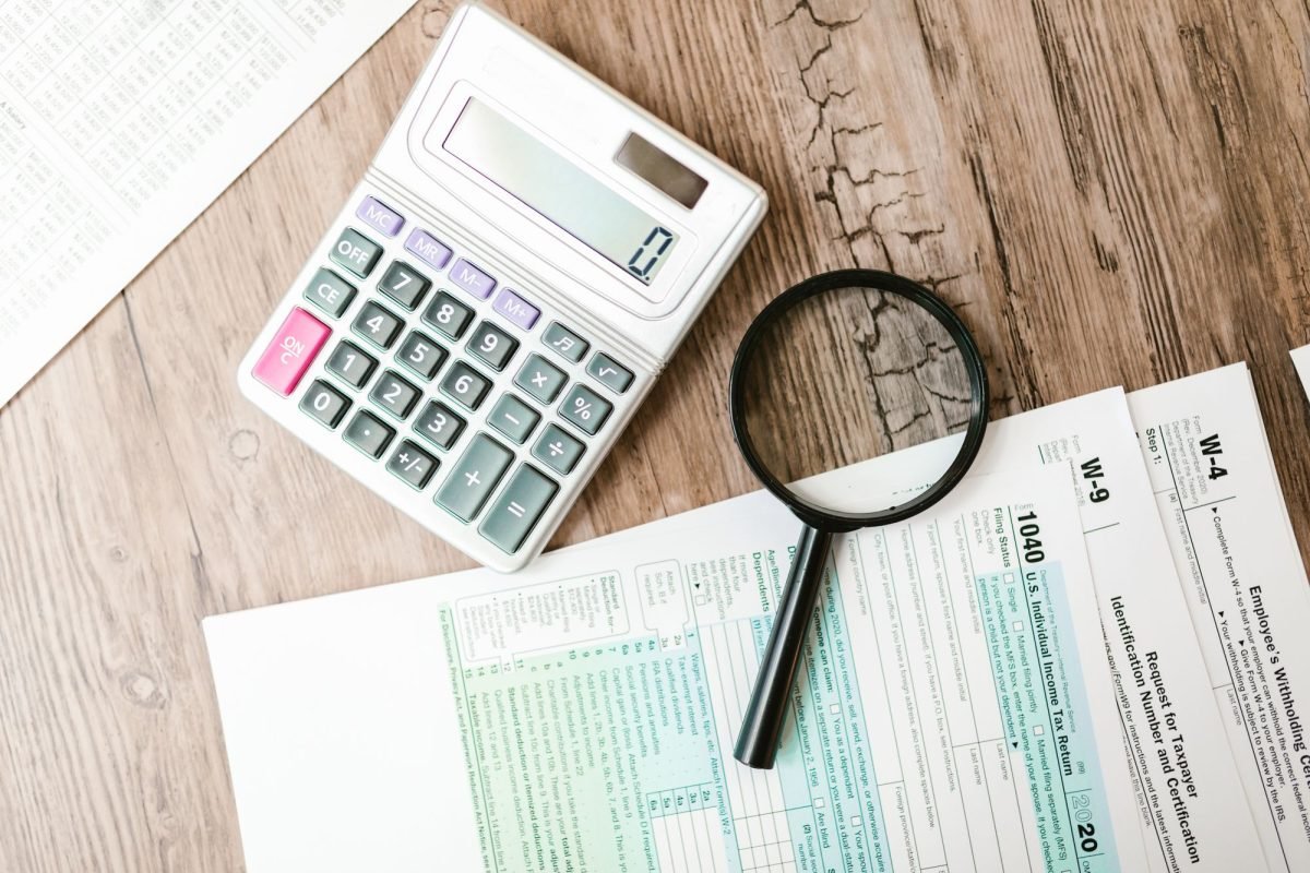A calculator and magnifying glass beside tax forms on a wooden surface