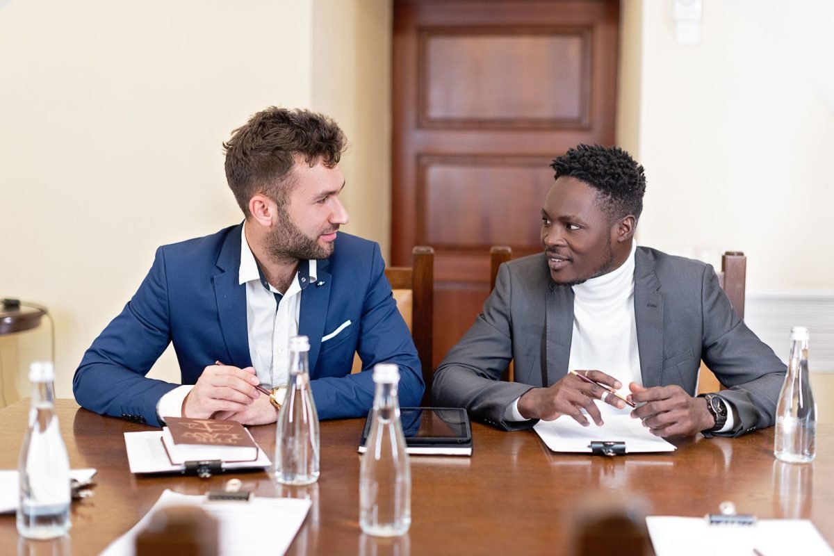 Two men in suits sitting beside each other at a conference table