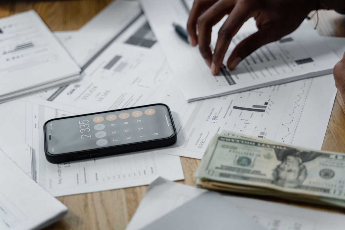 Hands calculating figures with reports, a smartphone and cash on a table