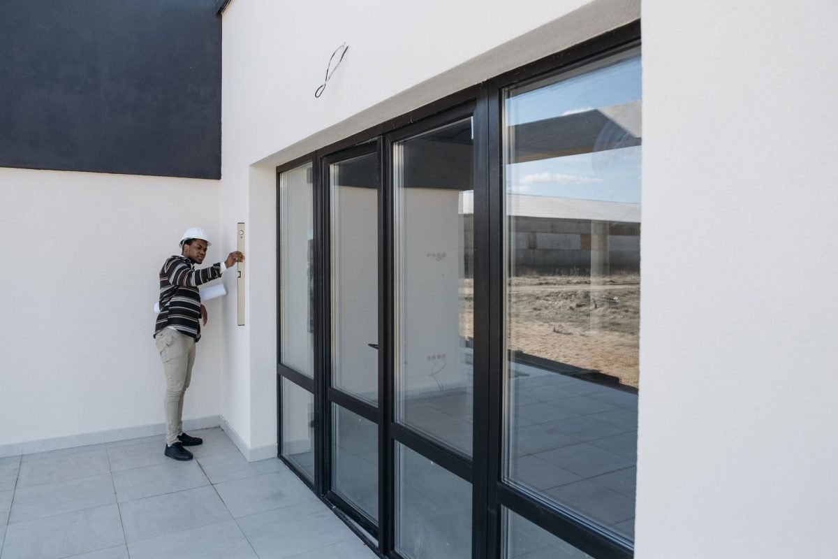 A professional in a hard hat inspecting a glass door in a house under construction