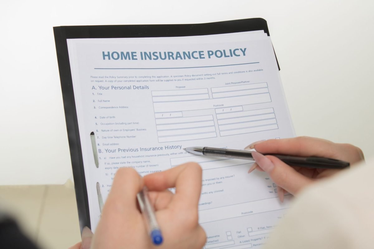 Hands holding pens and filling out a home insurance policy document