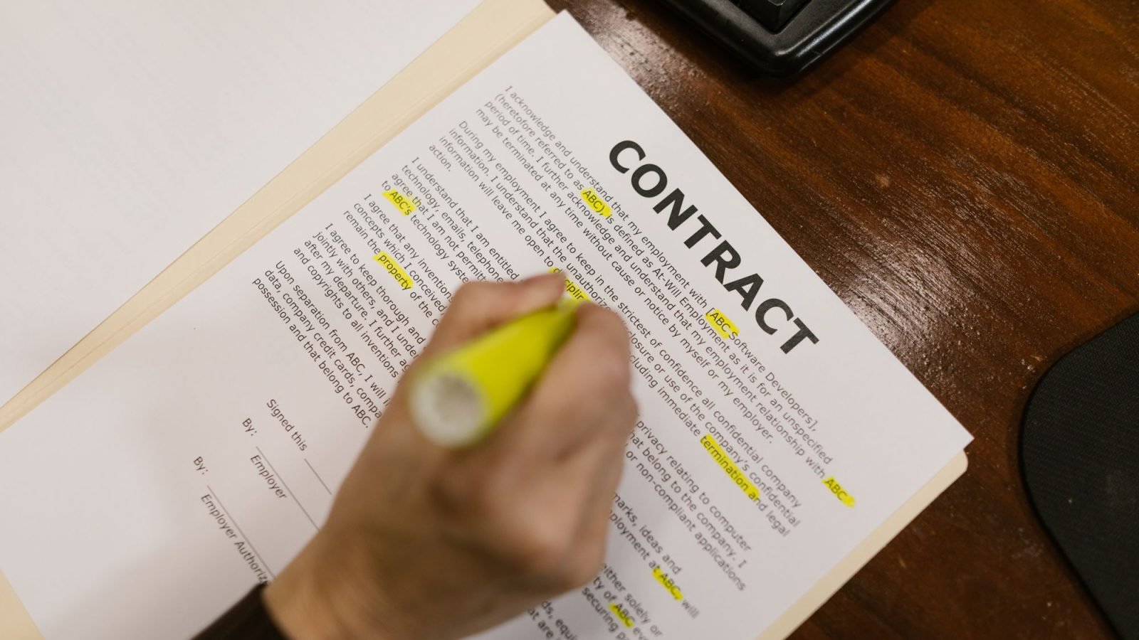 A person highlighting text in a contract on a wooden desk
