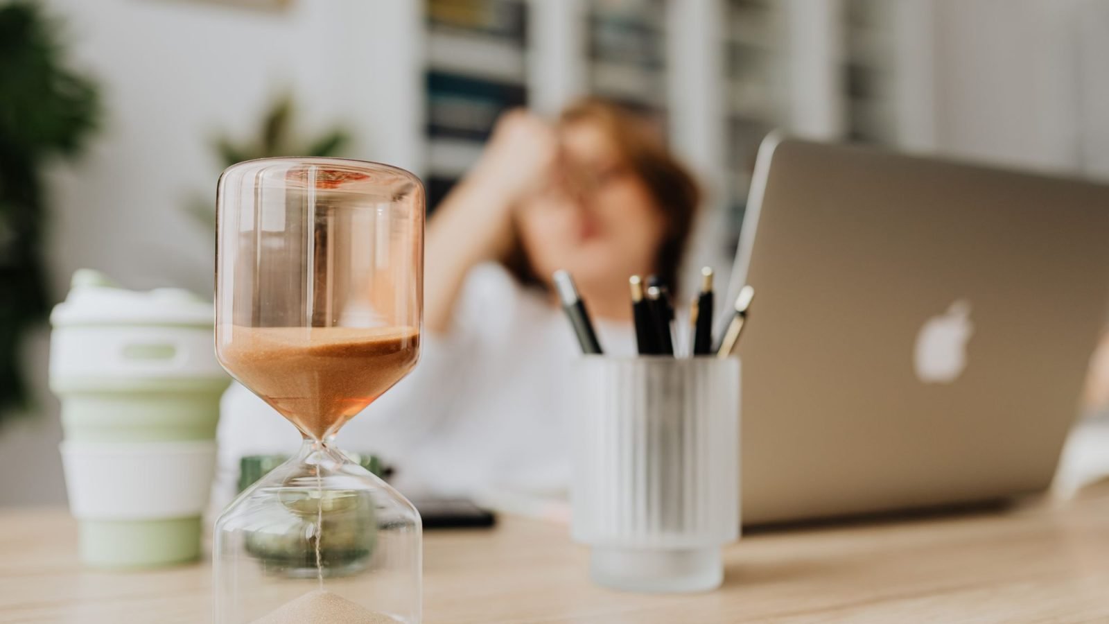 An hourglass on a desk in front of a laptop
