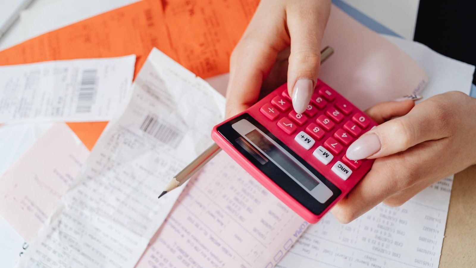 Hands using a pink calculator among receipts and documents