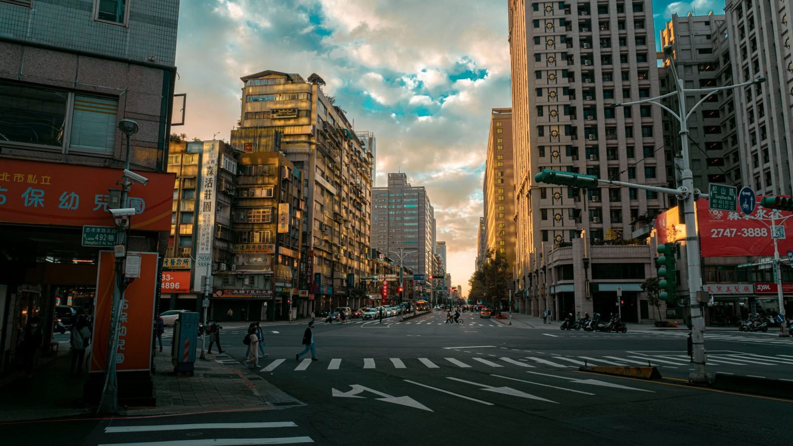 A city intersection at sunset with pedestrians and high-rise buildings