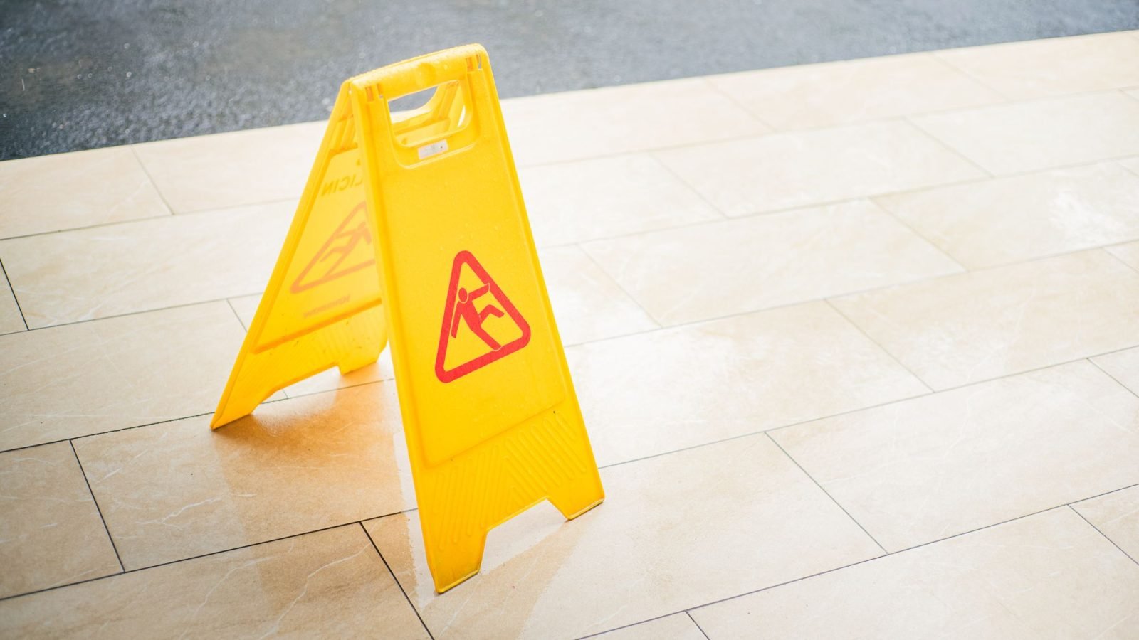 A bright yellow wet floor caution sign on a tiled floor