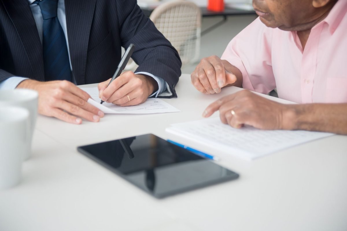 Hands of two men discussing and signing documents at an office table