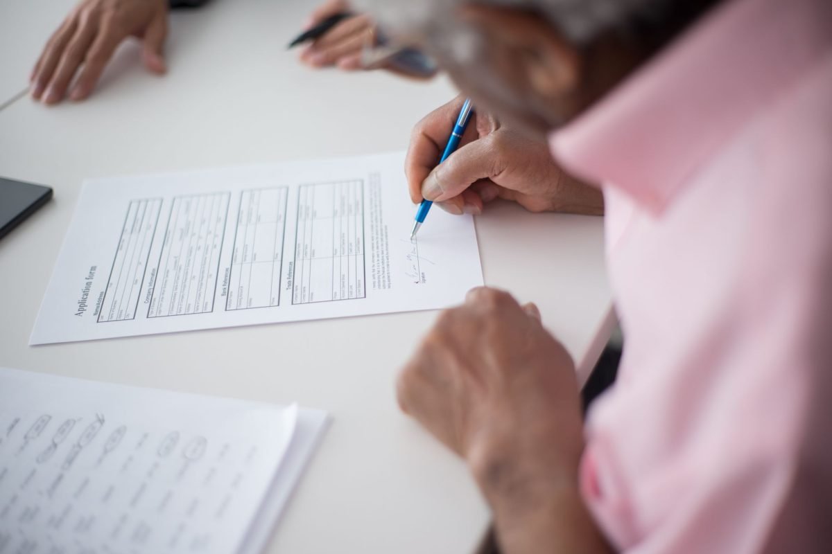 An older man signing a document at a desk in an office