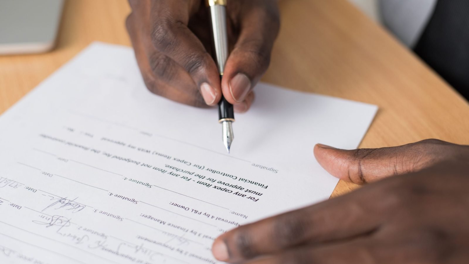 A man's hands signing a formal document indoors