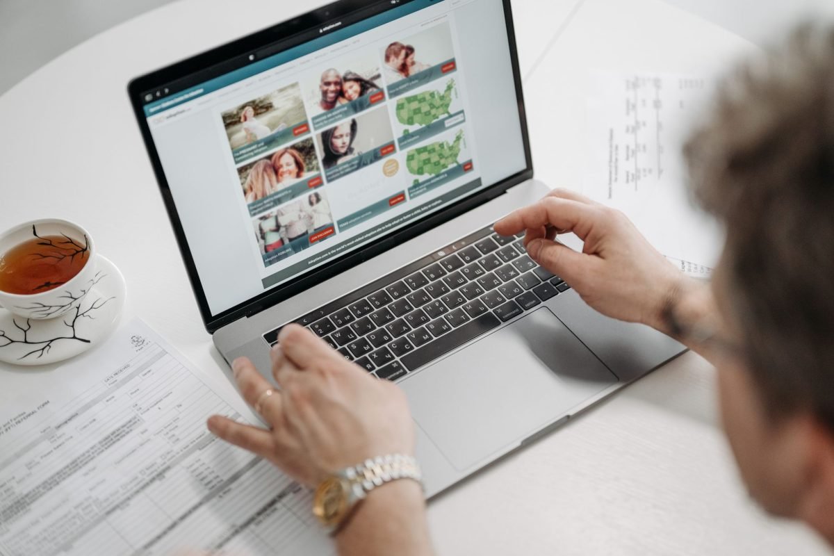A person browsing a website on a laptop with a cup of tea and documents on the table