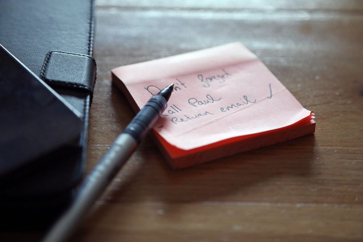 Sticky notes with a to-do list, a pen and a wallet on a wooden desk