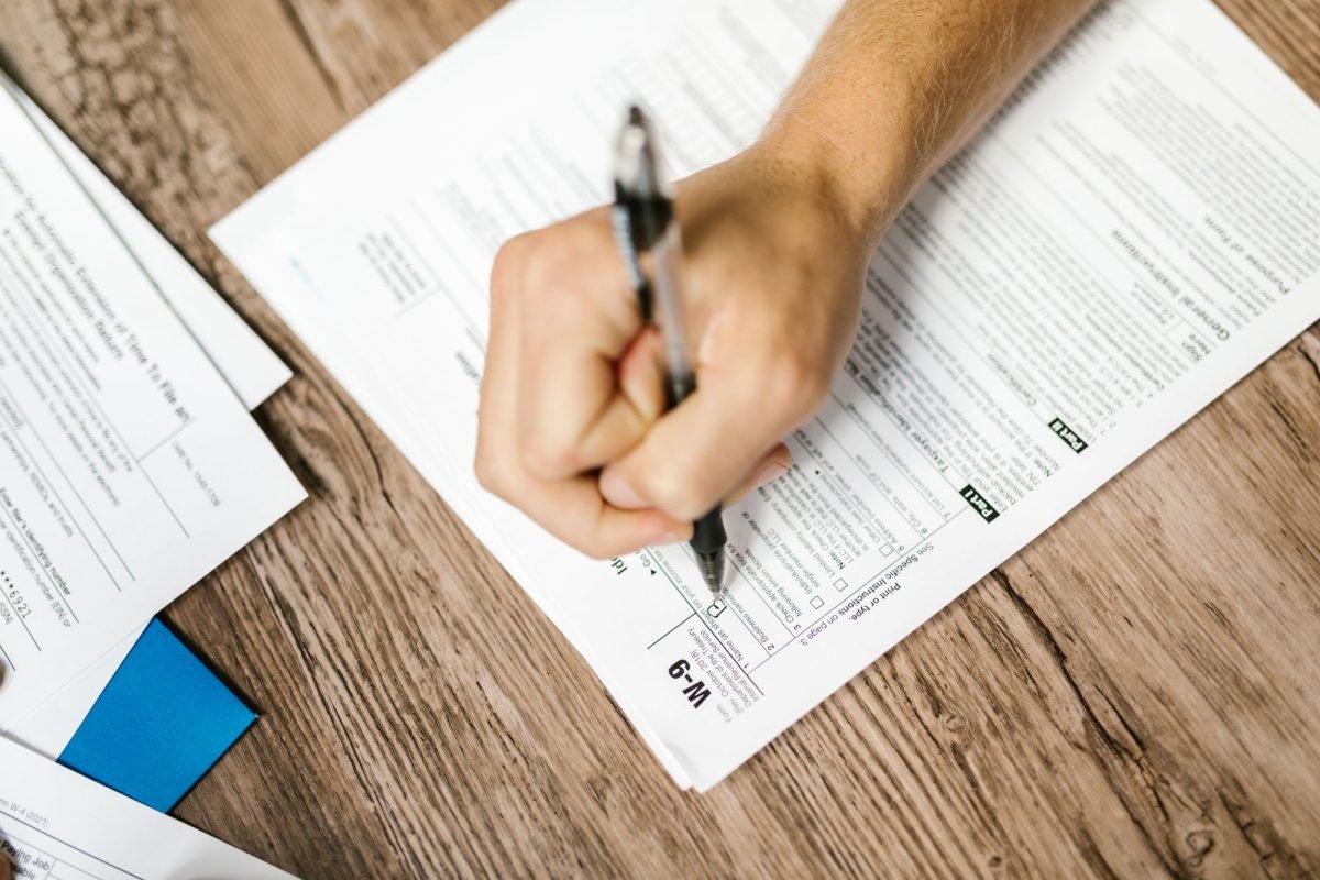 A hand writing on a tax form with a ballpoint pen