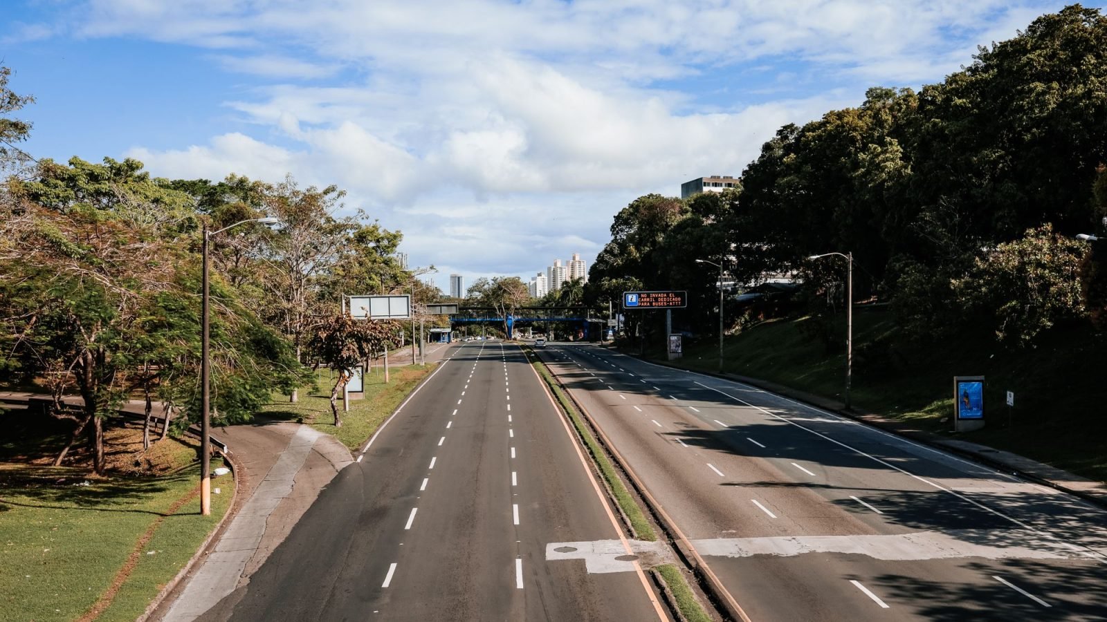 An empty highway lined with greenery under a blue sky