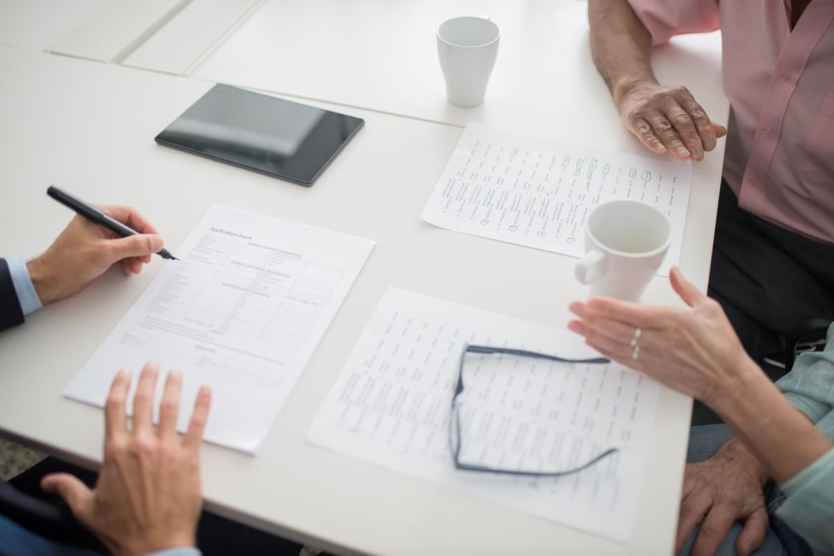 Hands writing on documents at a meeting table with coffee cups