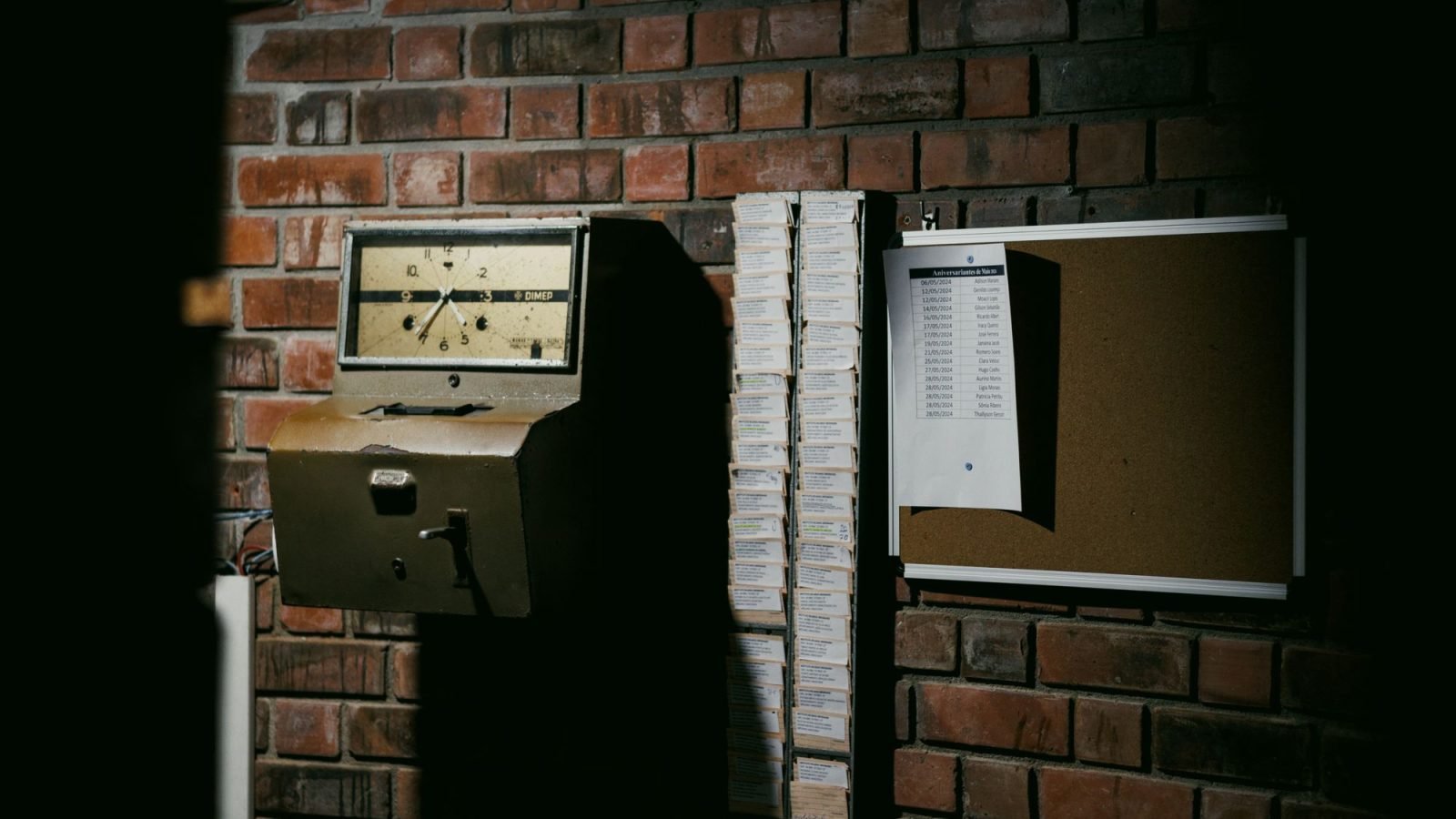 A retro time clock and punch cards against a brick wall