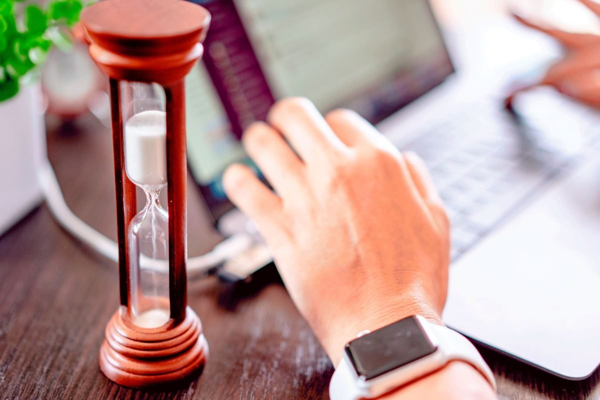 A hand on a laptop beside an hourglass