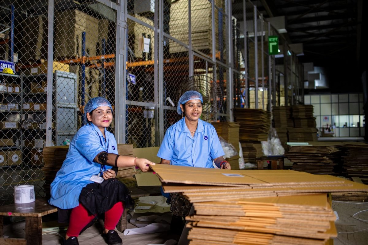 Two women in uniforms handling cardboard in a warehouse
