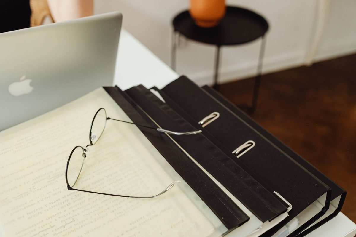 Eyeglasses resting on top of binders beside a laptop