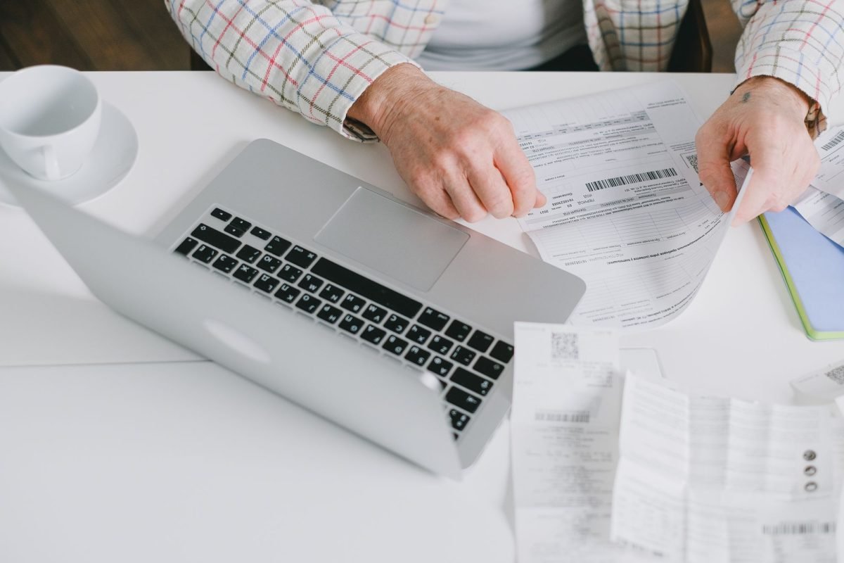 Hands organizing documents on a desk with a laptop