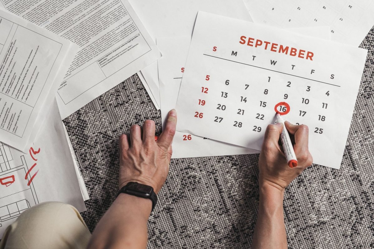 Hands holding a calendar with dates circled, with documents on the floor